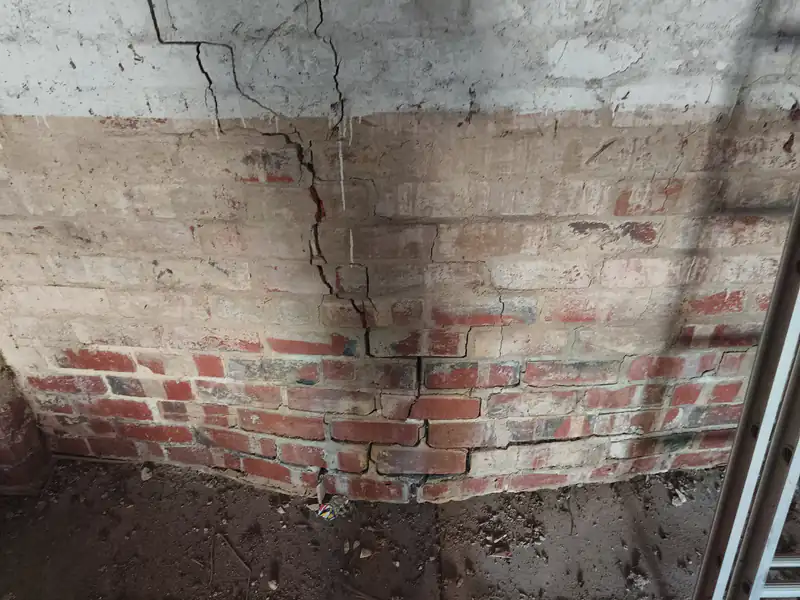 Cracking across a brick wall and its coated upper section.