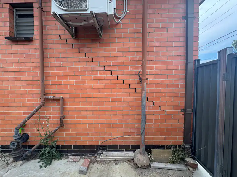 Stepped cracking in brickwork beside services and an external air-conditioning unit.