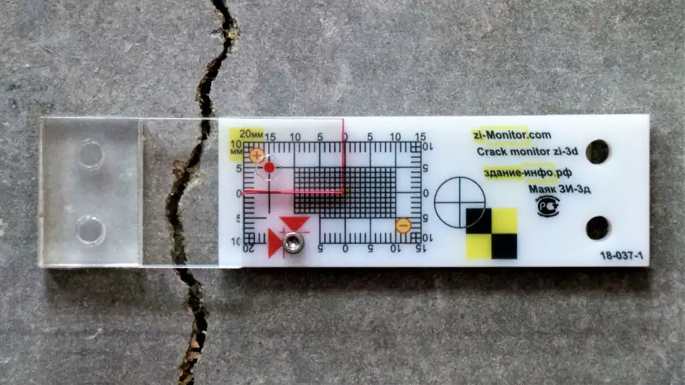 A crack-monitoring gauge spanning a crack in a concrete surface.